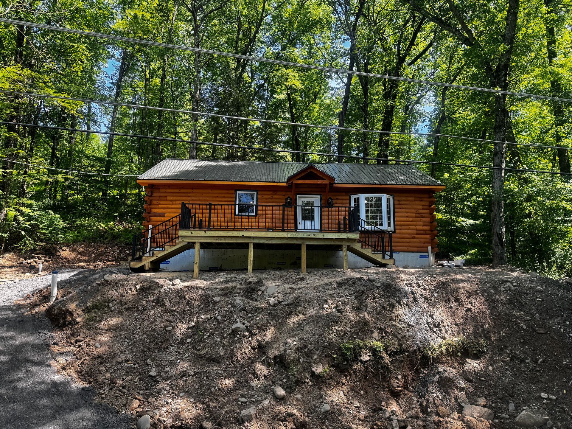 A small log cabin is sitting on top of a dirt hill in the middle of a forest.