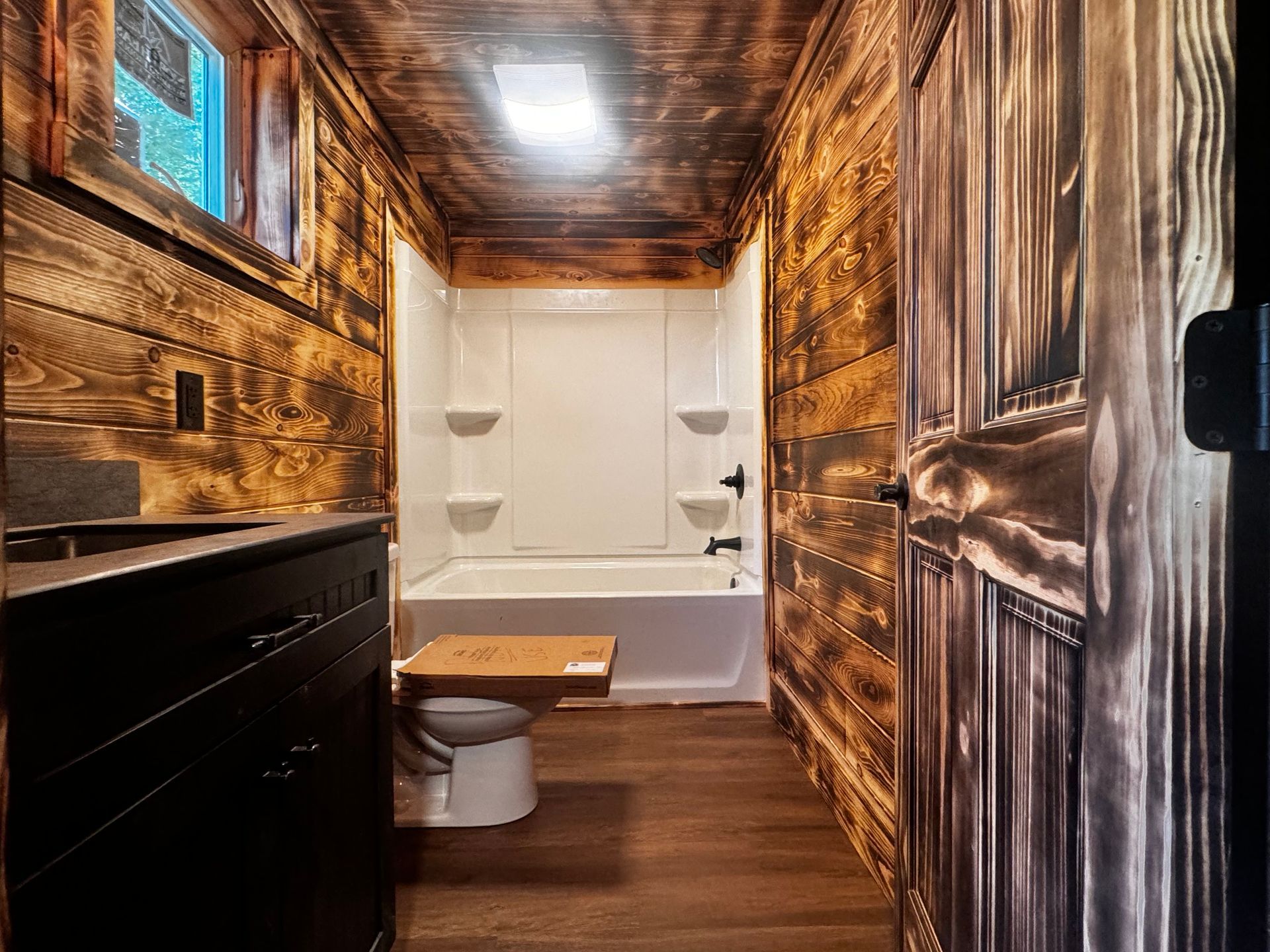 A bathroom with a toilet , tub , shower and wooden walls.