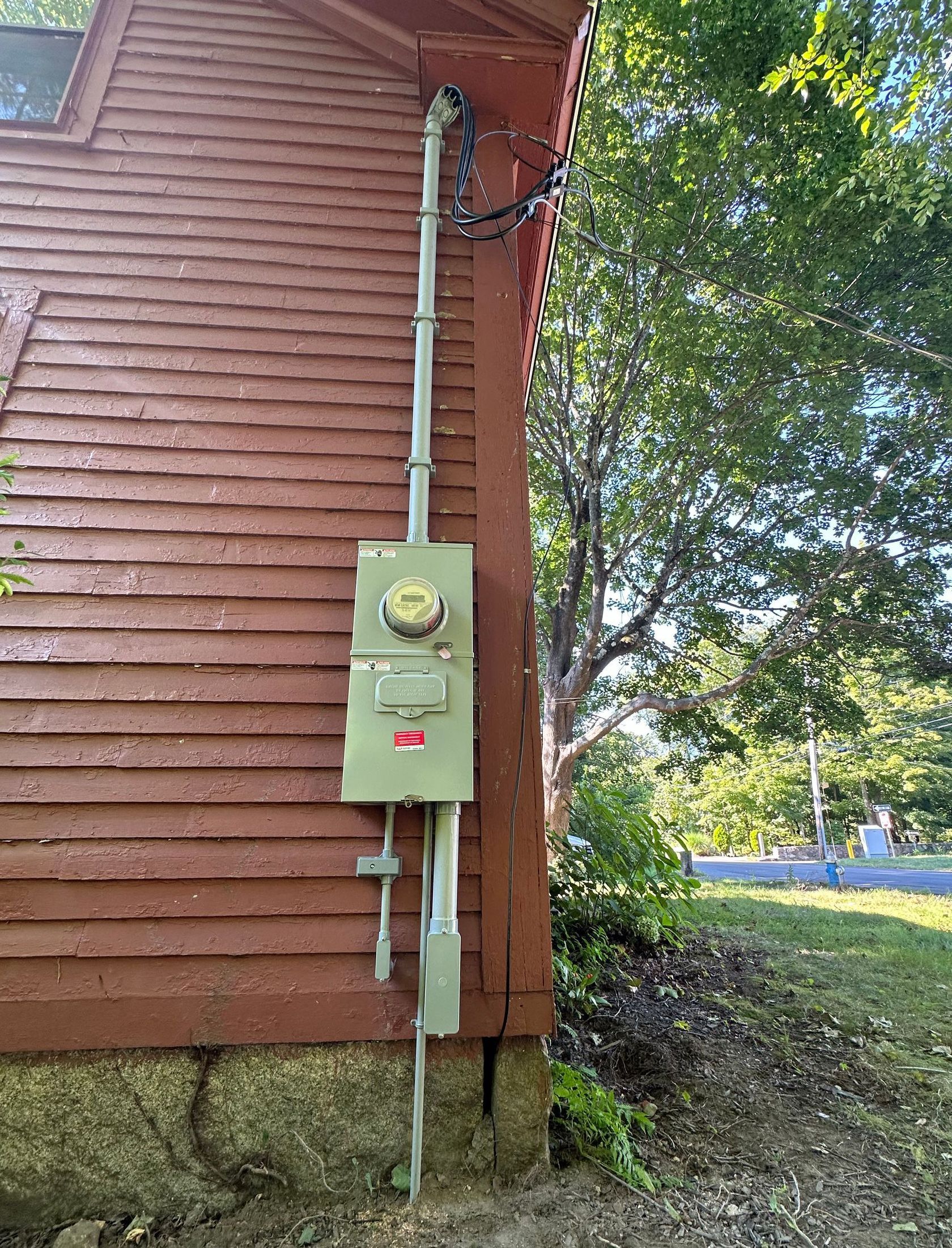 A red wooden building with an outdoor electrical meter and conduit. The meter is green and mounted vertically on the side of the structure.