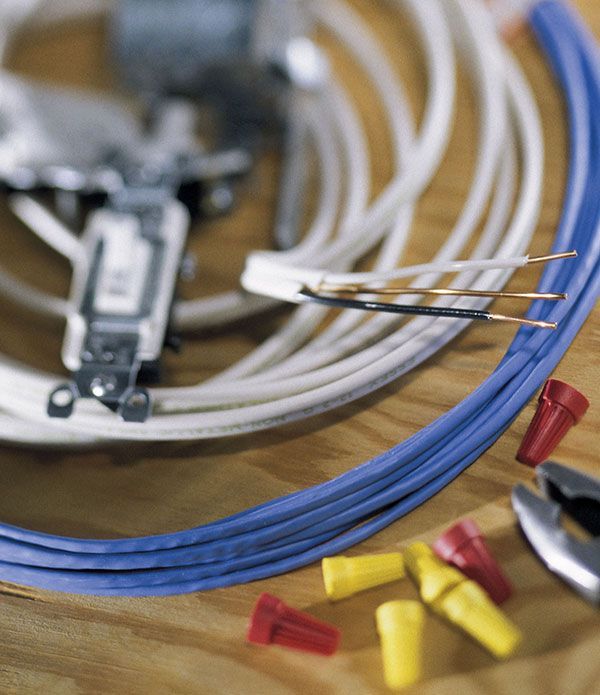 Electrical wiring materials including a light switch, wires, wire connectors, and pliers on a wooden surface.