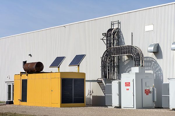Yellow generator with solar panels next to a white industrial building with conduit and electrical boxes.