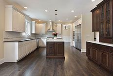 A kitchen with white and dark brown cabinets, a central island, stainless steel appliances, and dark wooden floors.
