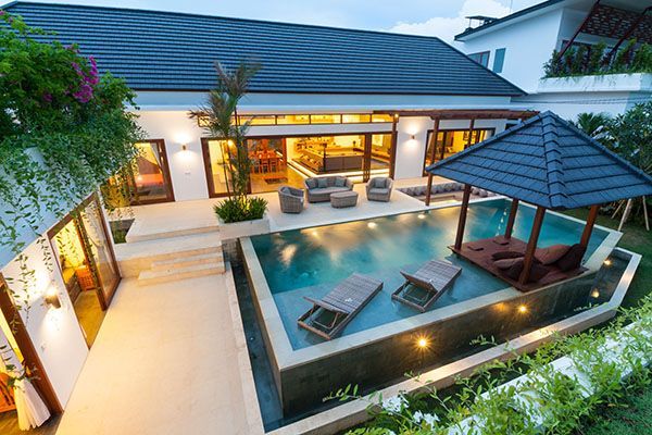 Modern villa with a pool and a gazebo. Blue tile roof, white walls, and lounge chairs in water.