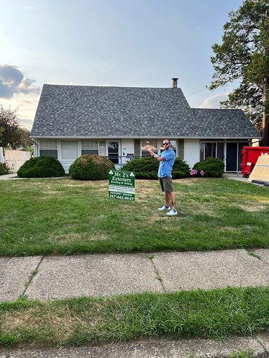 A man is standing in front of a house with a sign in the grass.