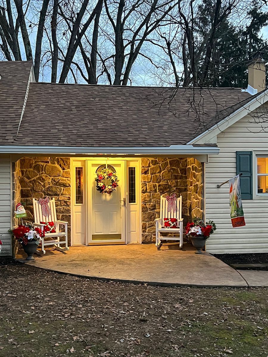 The front of a house decorated for christmas with rocking chairs and a wreath on the door.