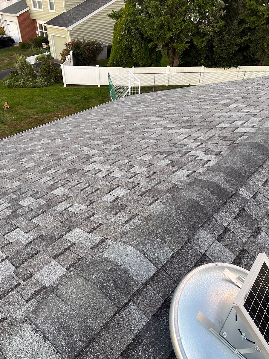 A close up of a roof with shingles and a fan on it.