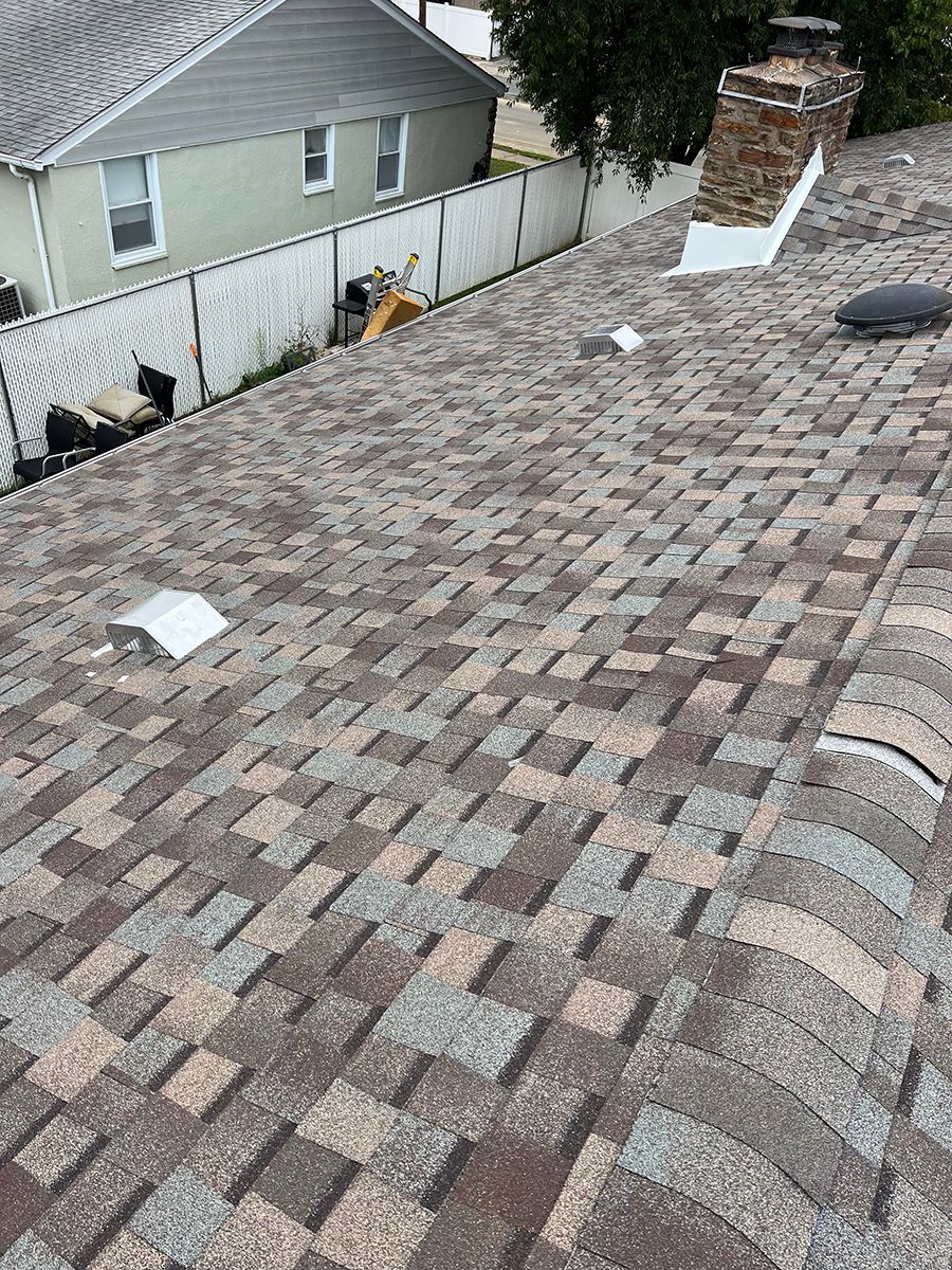 A close up of a roof with a chimney and a house in the background.