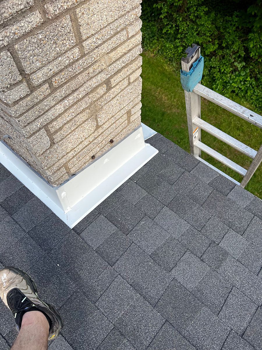 A person is standing on a roof next to a chimney.