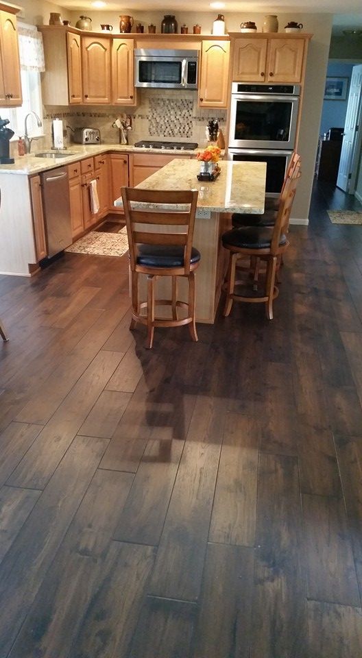 A kitchen with hardwood floors , wooden cabinets , stainless steel appliances and a large island.