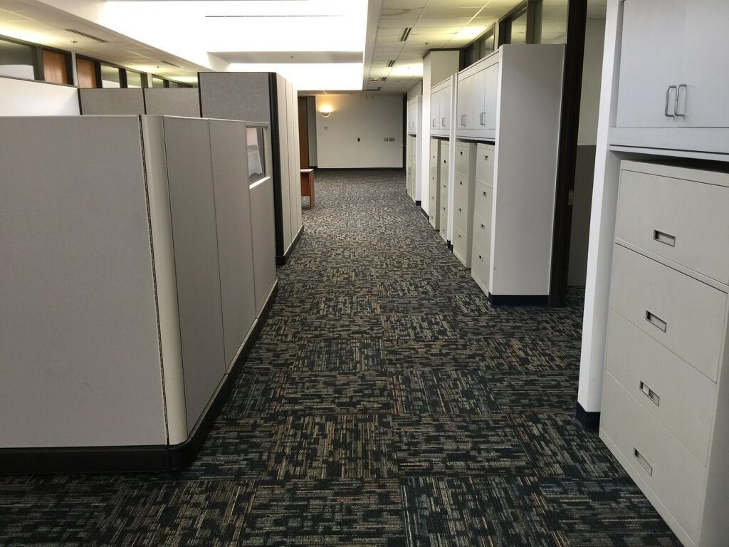 A long hallway with cubicles and filing cabinets in an office building.