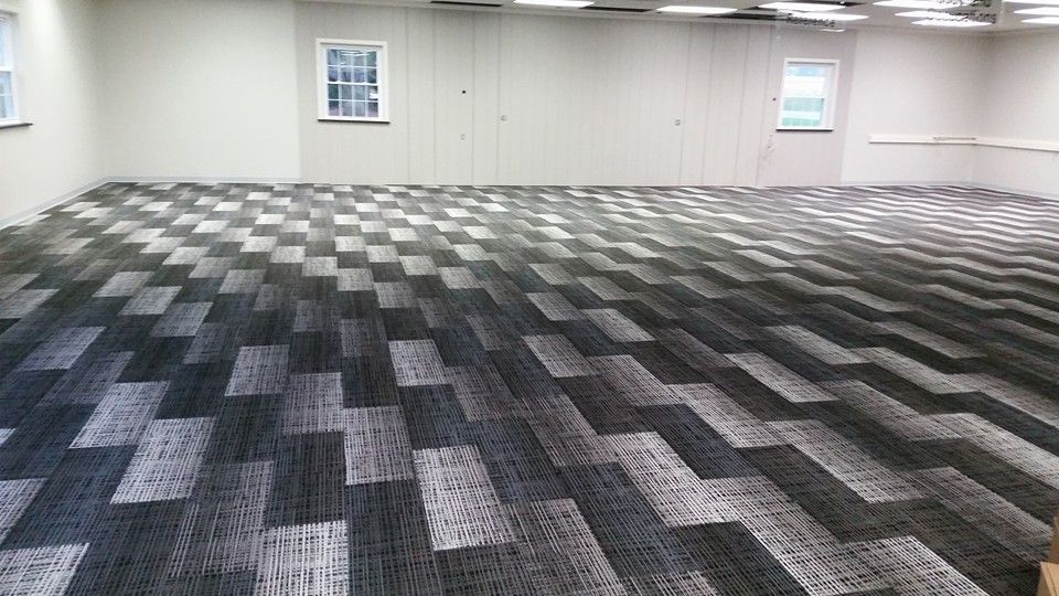 A large room with a carpeted floor and two windows.