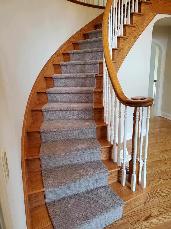 A curved staircase with a gray carpet and a wooden railing.