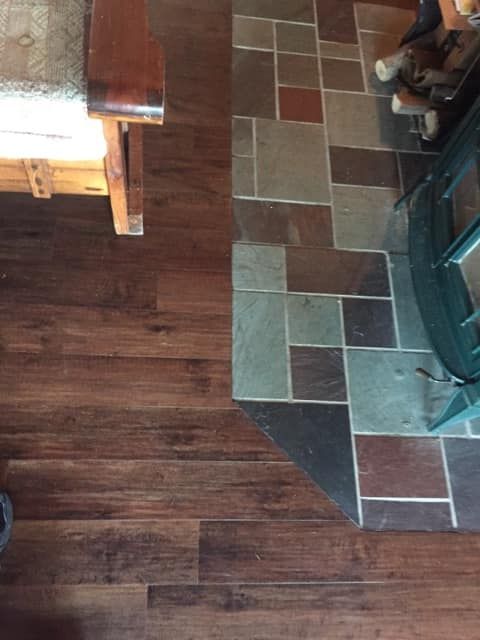 A wooden floor next to a tiled floor and a fireplace.