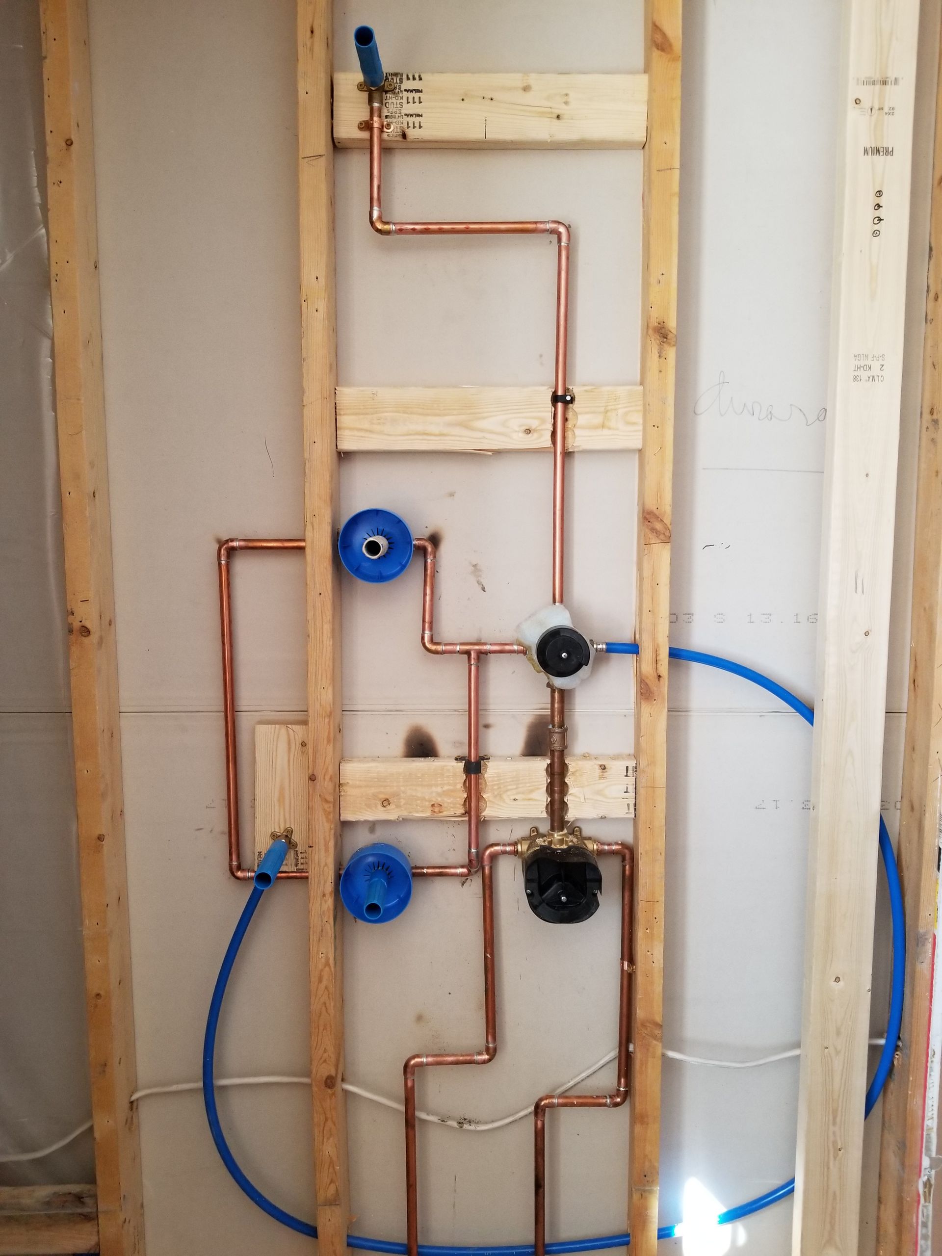 Exposed copper and blue plumbing lines inside an unfinished wall frame.