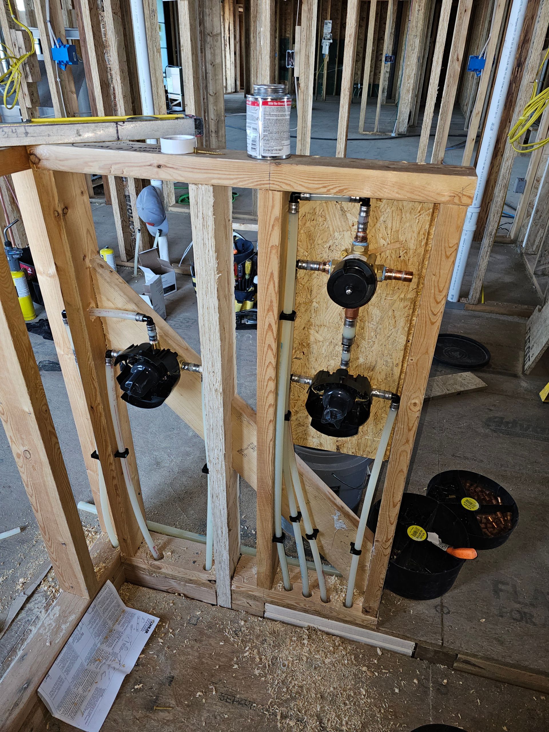Framed electrical wall with wires, outlets, and a black bucket on a construction site