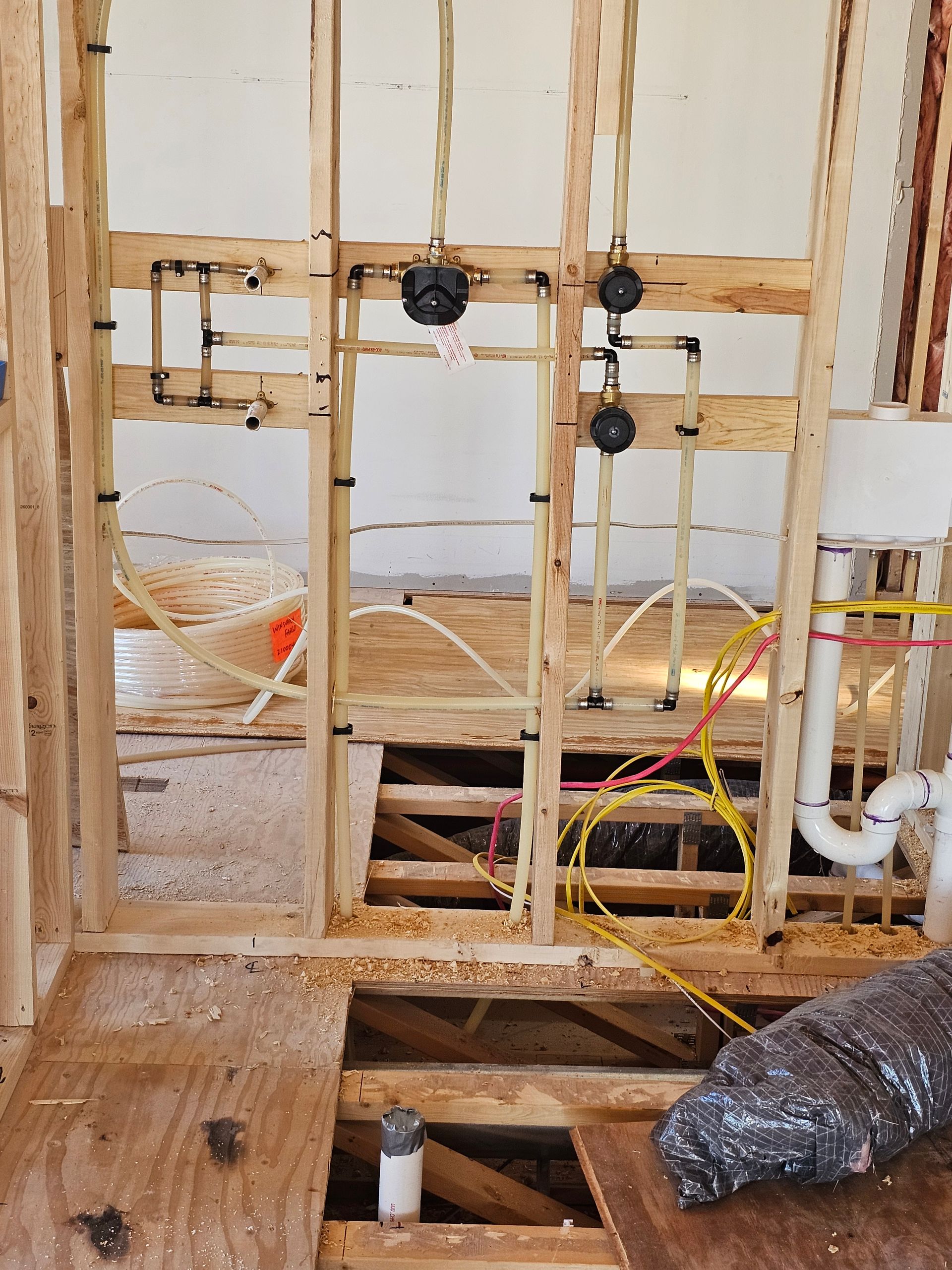 Exposed wall studs and plumbing in a home under renovation, with open floor framing and electrical wiring.