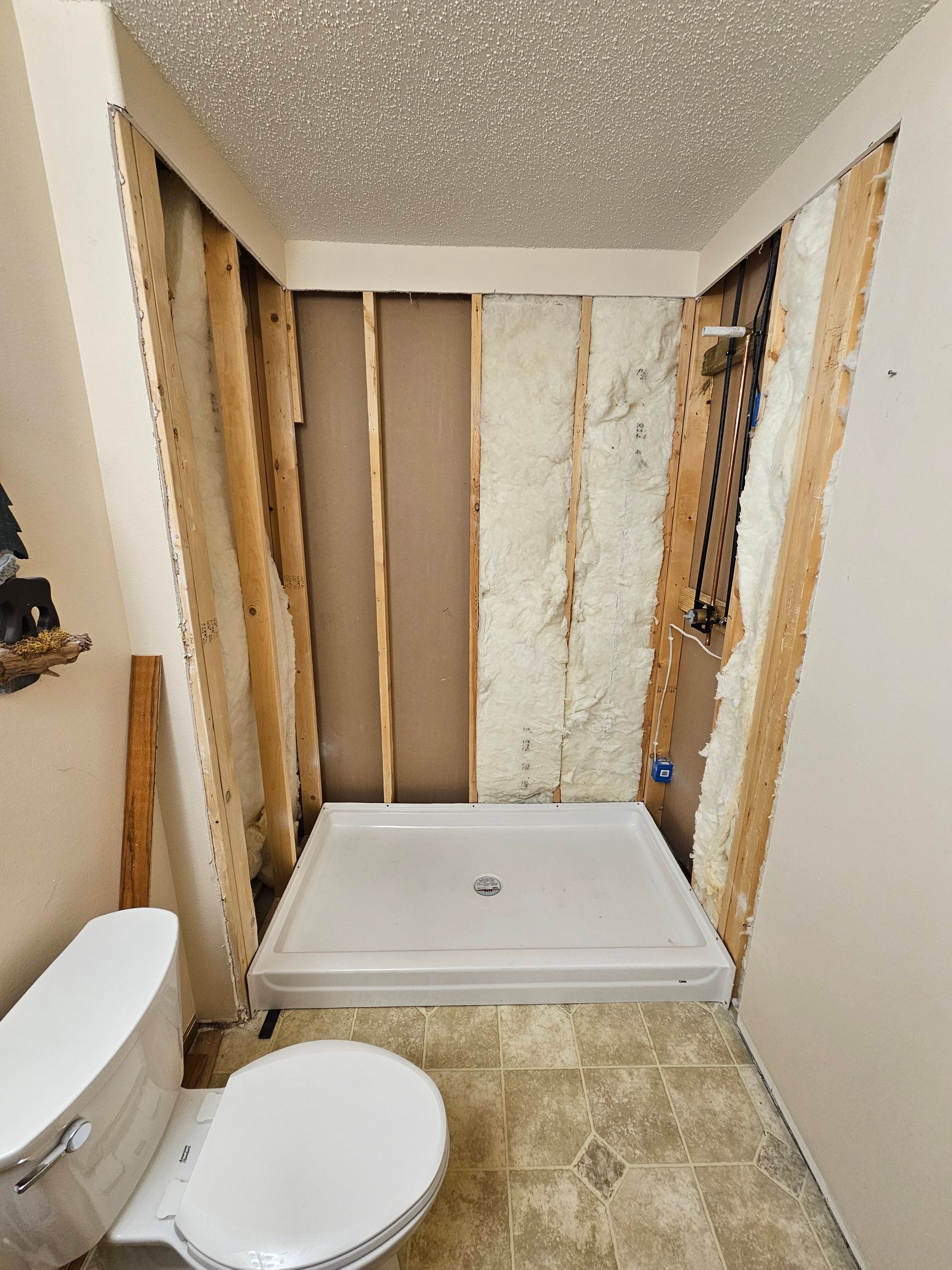 Partially renovated bathroom with exposed wall studs, toilet, and shower base under construction