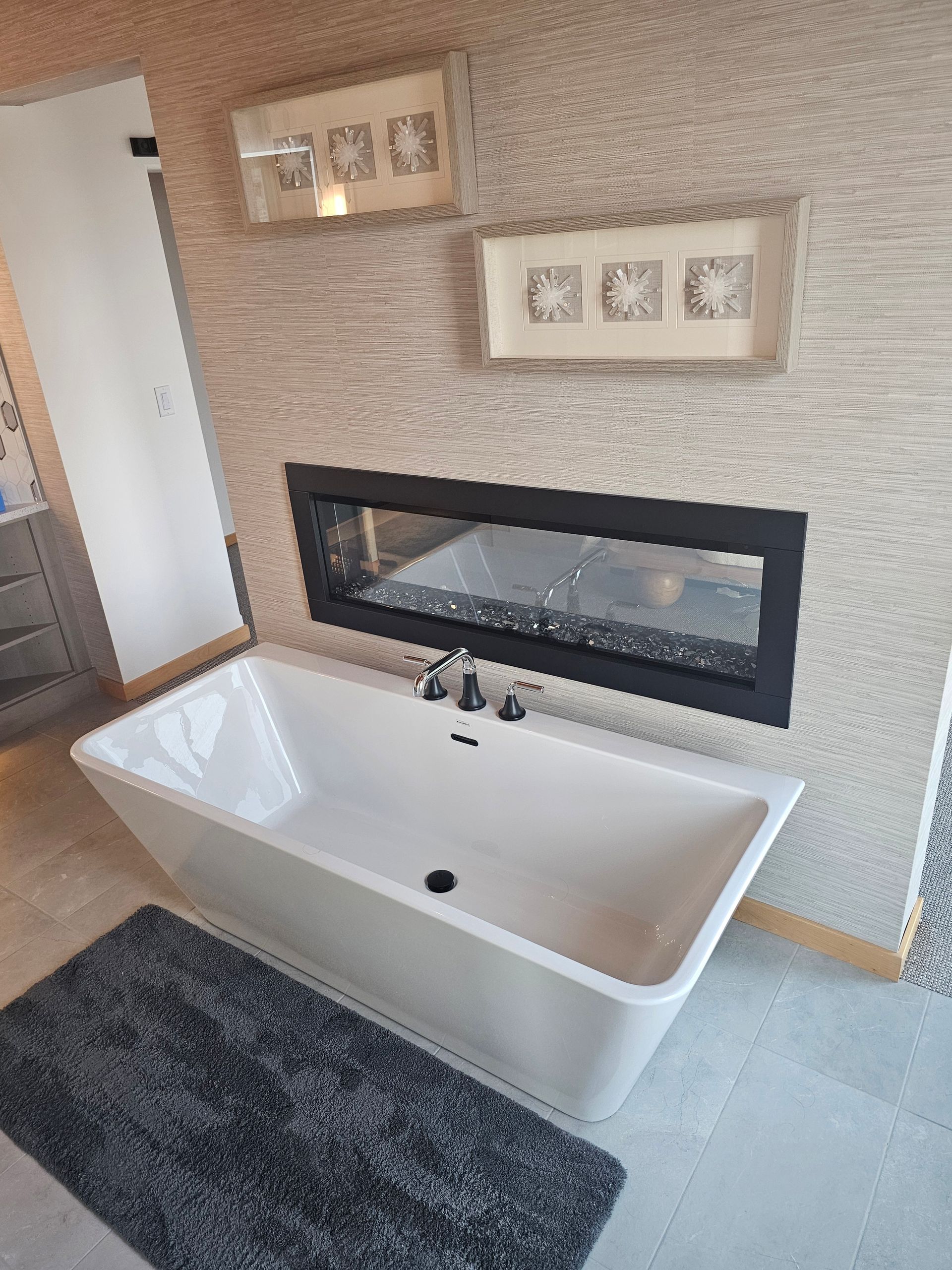Modern bathroom with a freestanding white tub, black rug, and decorative wall shelves above a long mirror