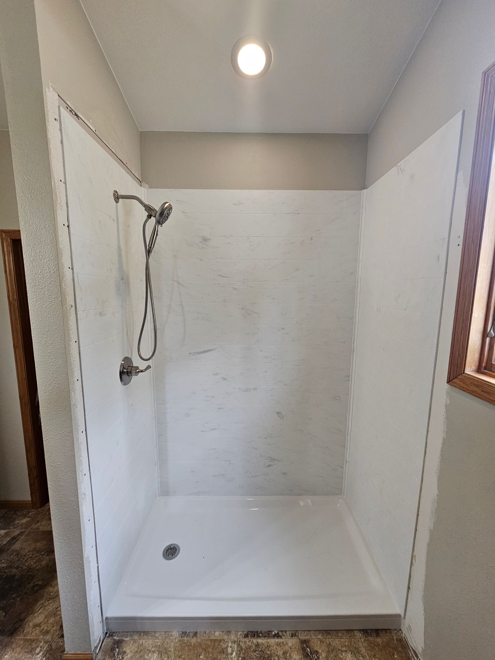 Small white shower stall with handheld showerhead and window on the right.