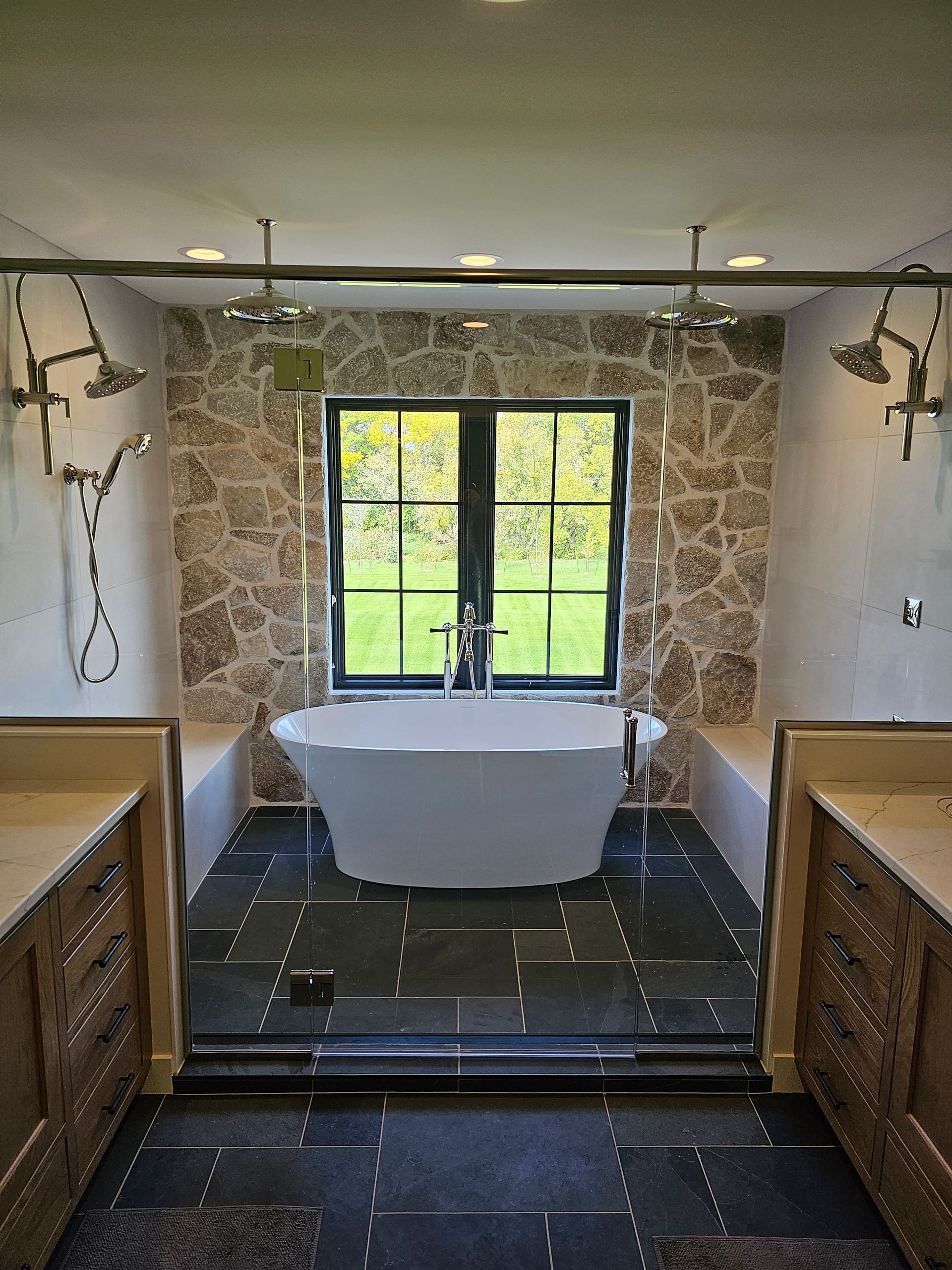 Elegant bathroom with a freestanding tub, stone walls, dark floor, and window overlooking greenery
