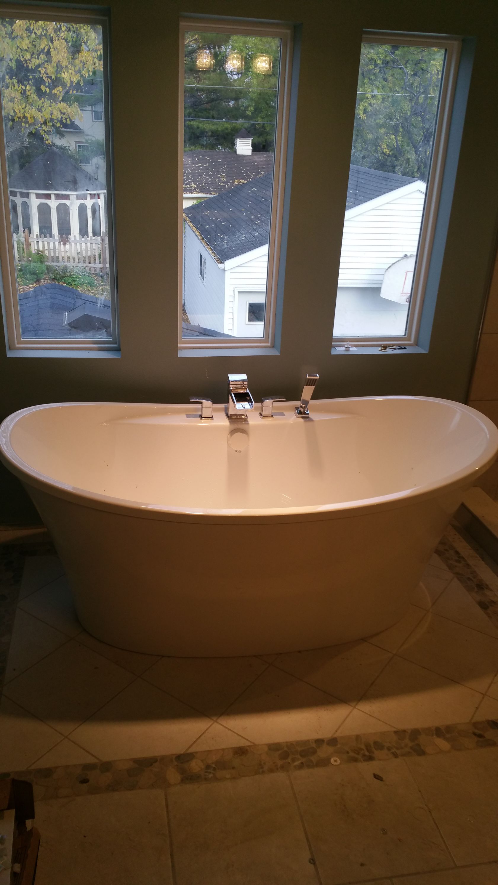 Bathroom sink beneath three windows, with a view of rooftops and trees outside.