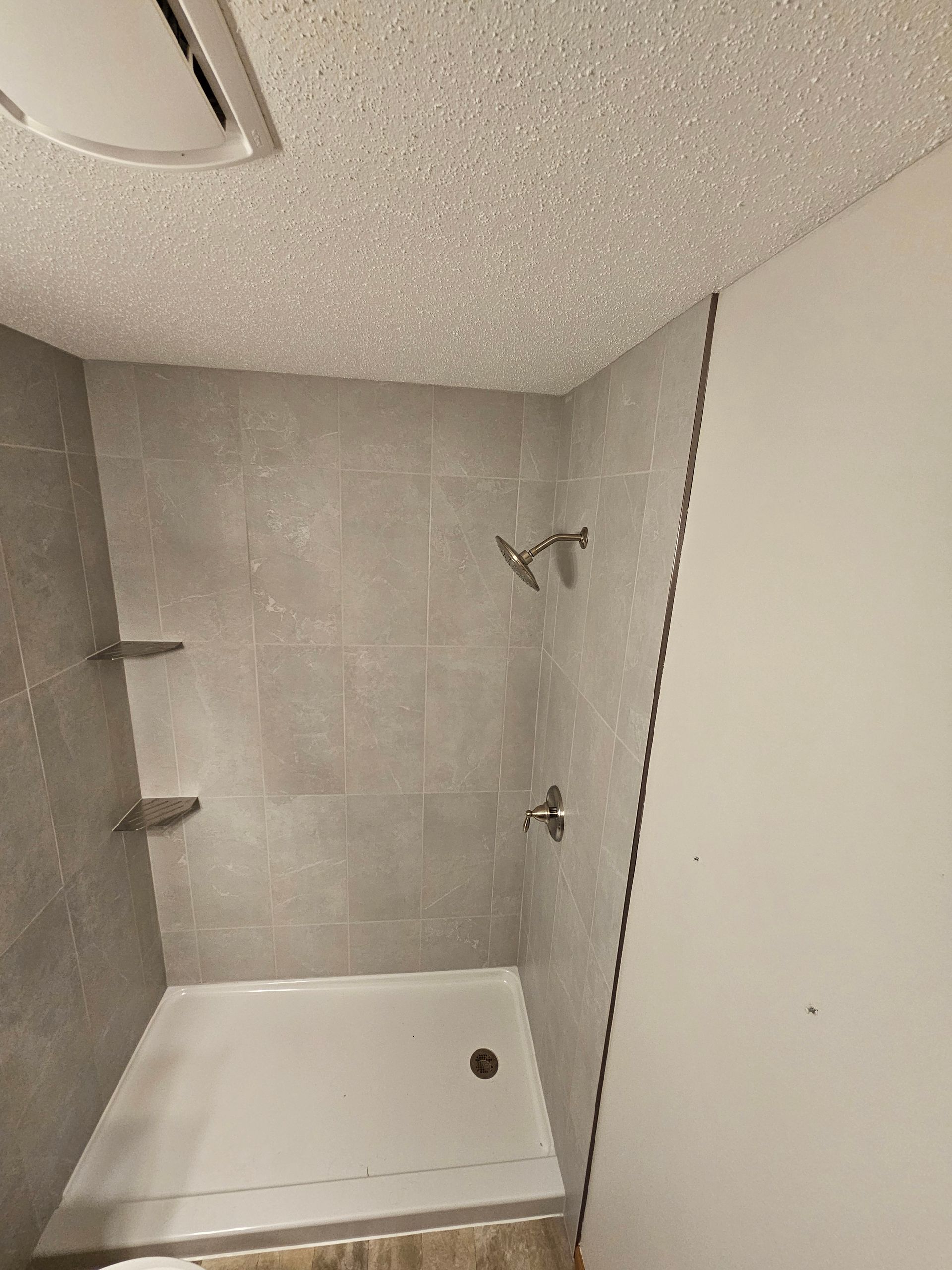 Small shower stall with white tub, gray tile walls, and built-in shelves.