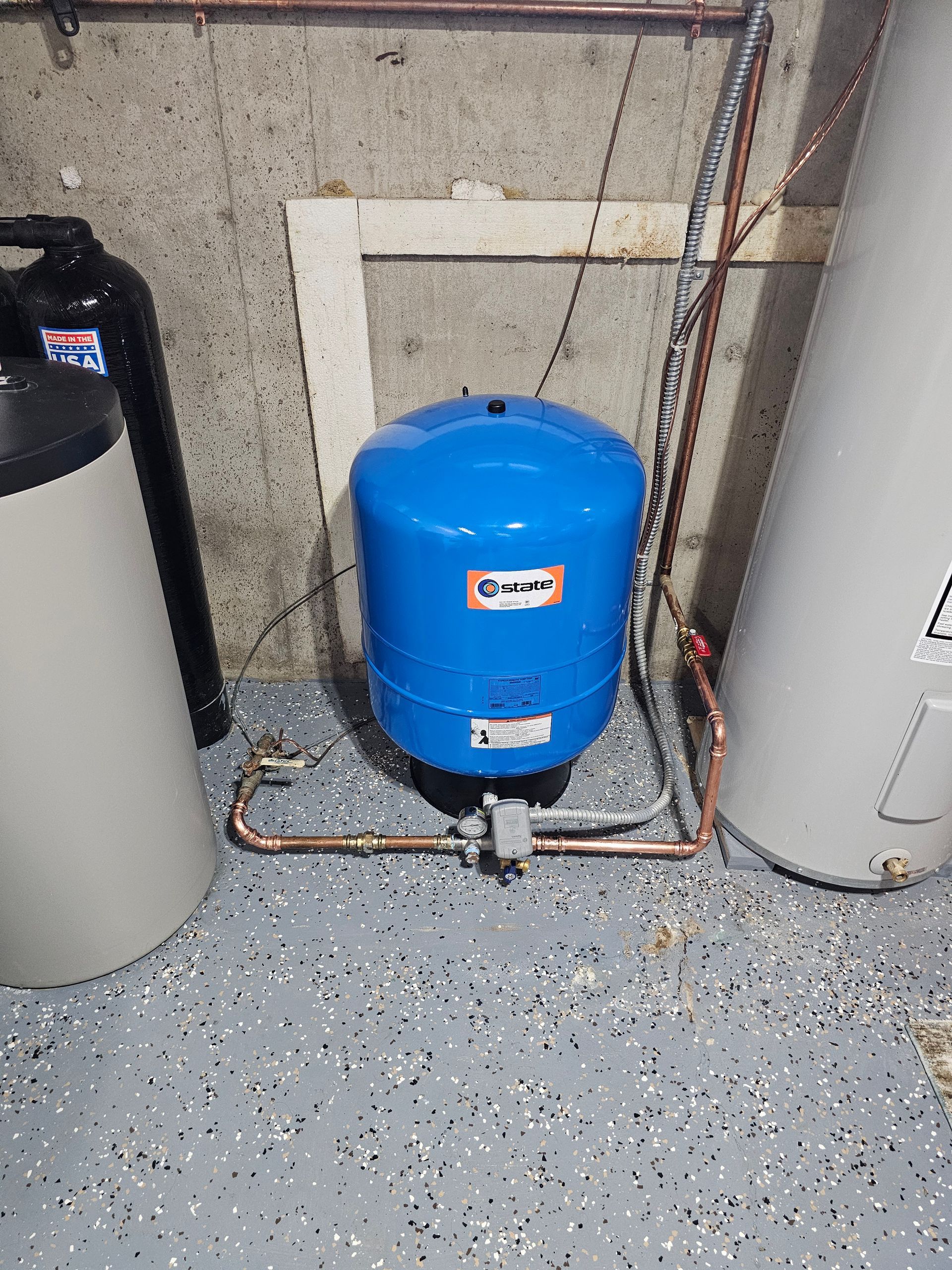 Blue pressure tank among utility pipes in a basement corner.