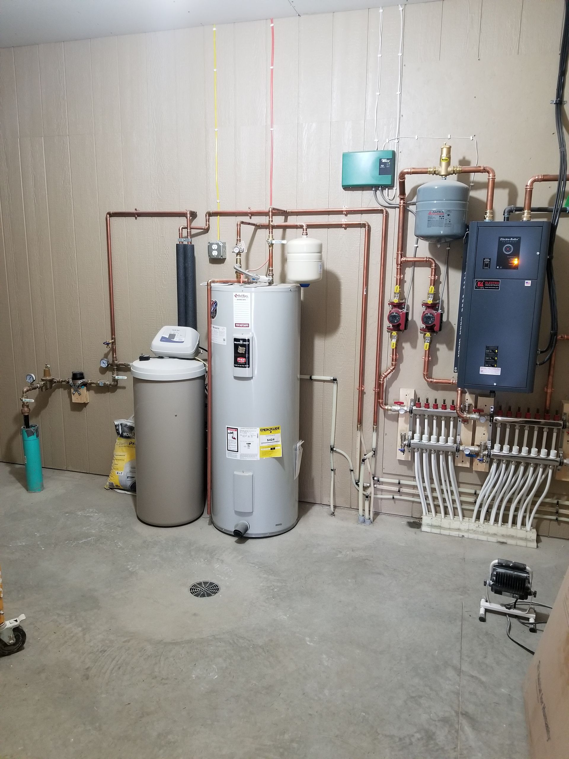 Utility room with water heaters, pipes, and a furnace against a concrete wall