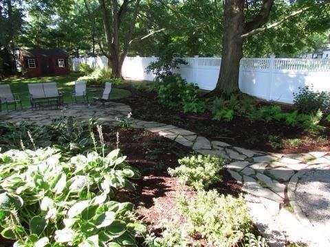 a stone walkway in a garden with a white fence in the background