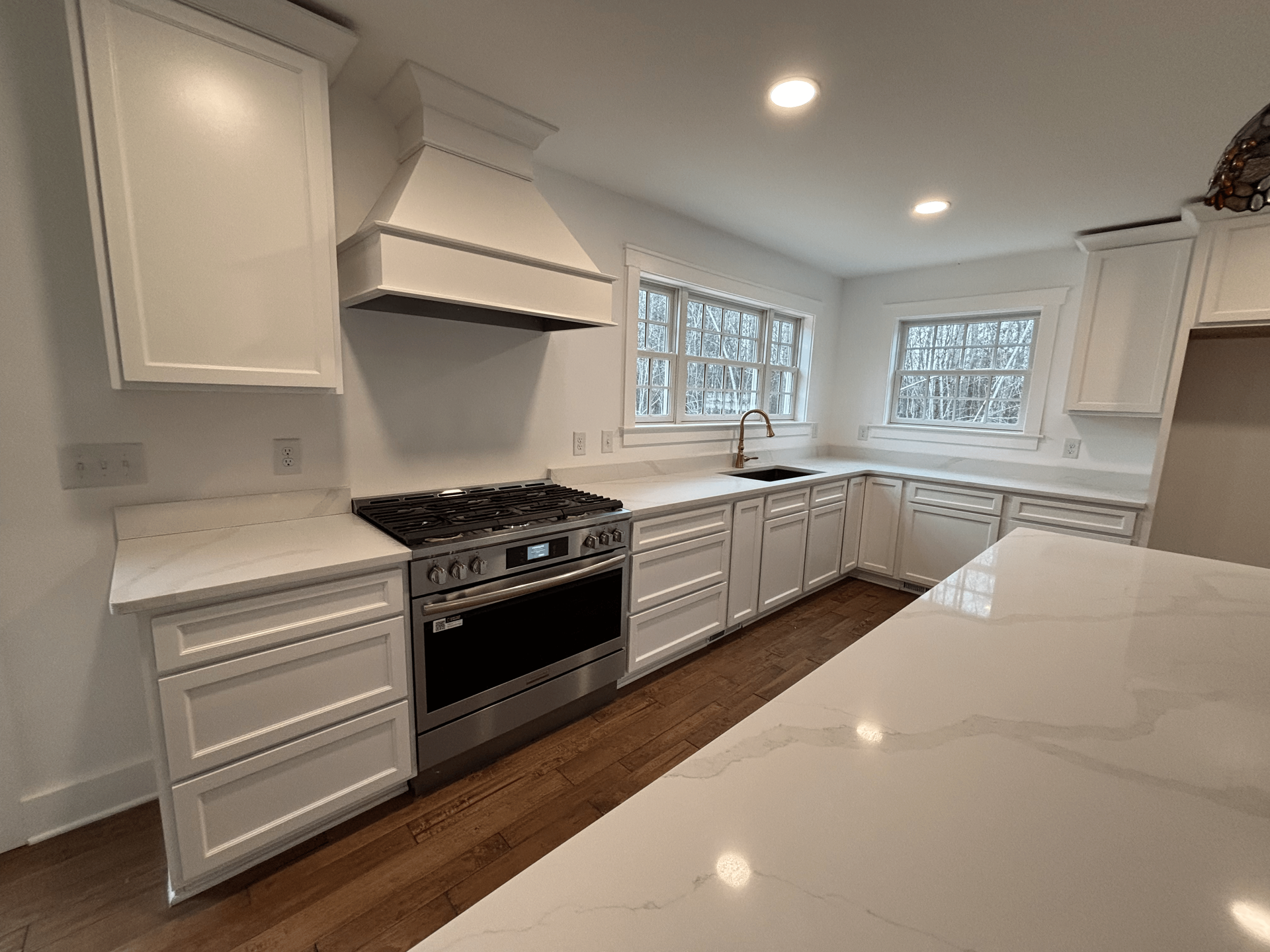 White kitchen with stainless steel appliances, white cabinets, and countertops, and wooden floors.
