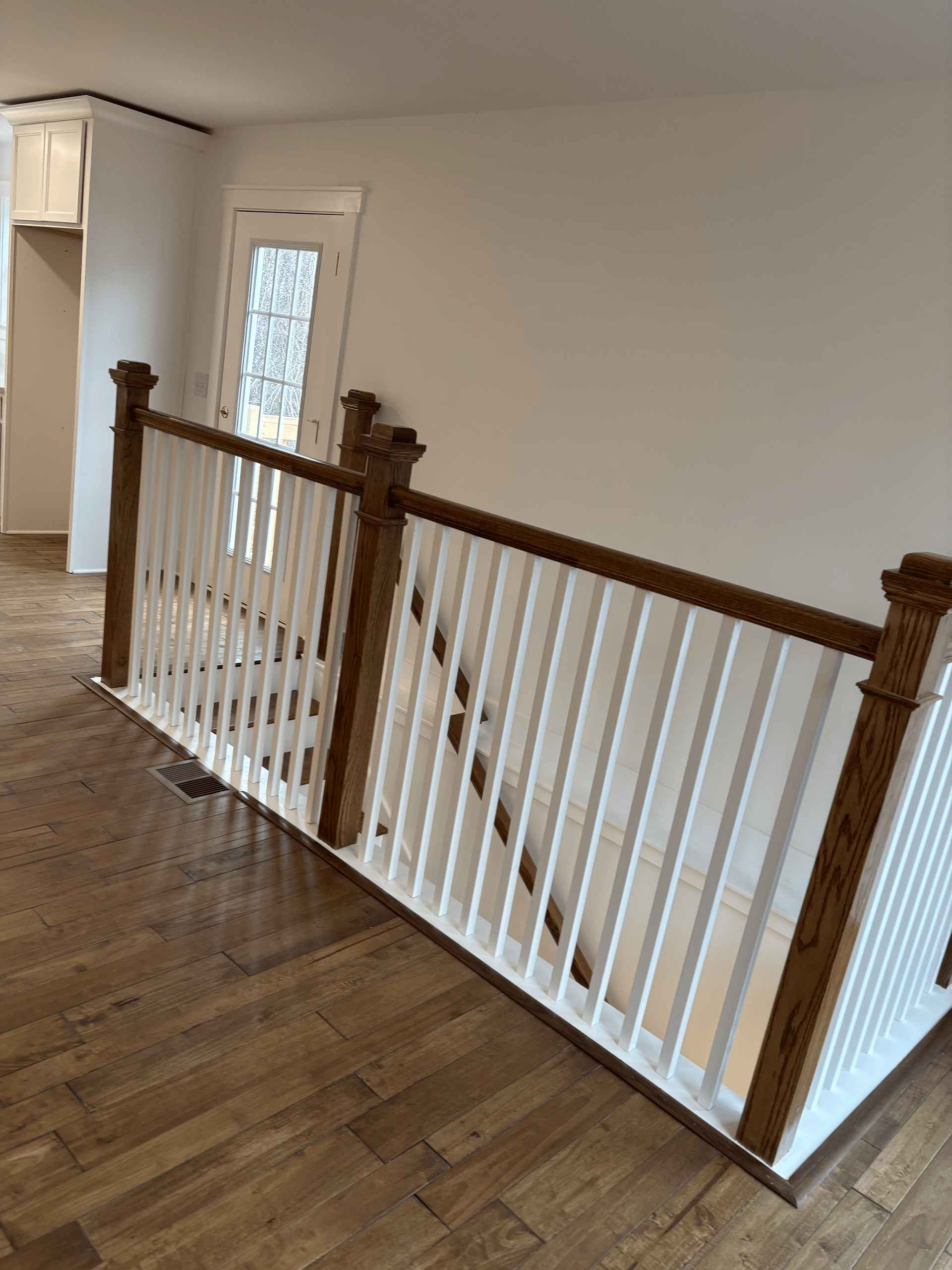 Wooden staircase with white spindles, brown handrails and trim, leading down.