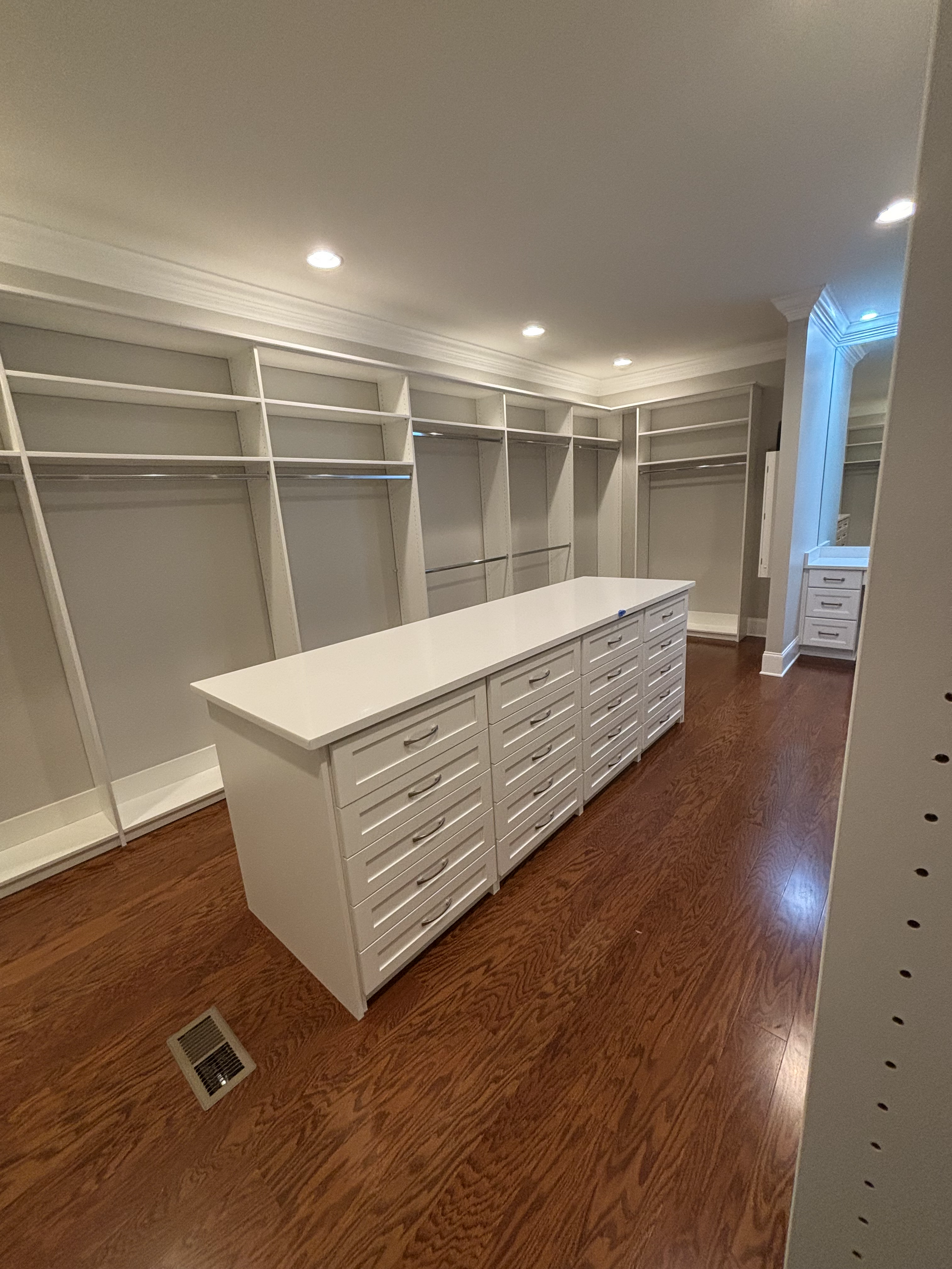 White walk-in closet with island of drawers, wood floor, empty shelves, and recessed lighting.