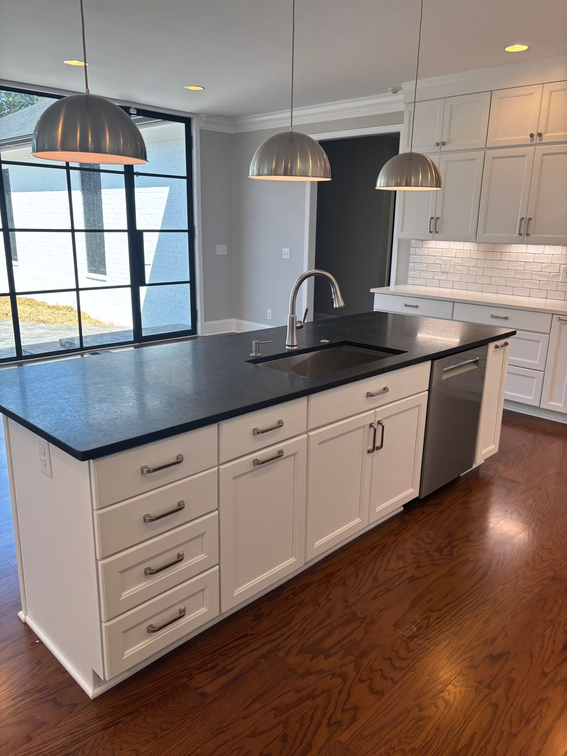 Modern kitchen with white cabinets, dark island countertop, stainless steel appliances, and pendant lights.