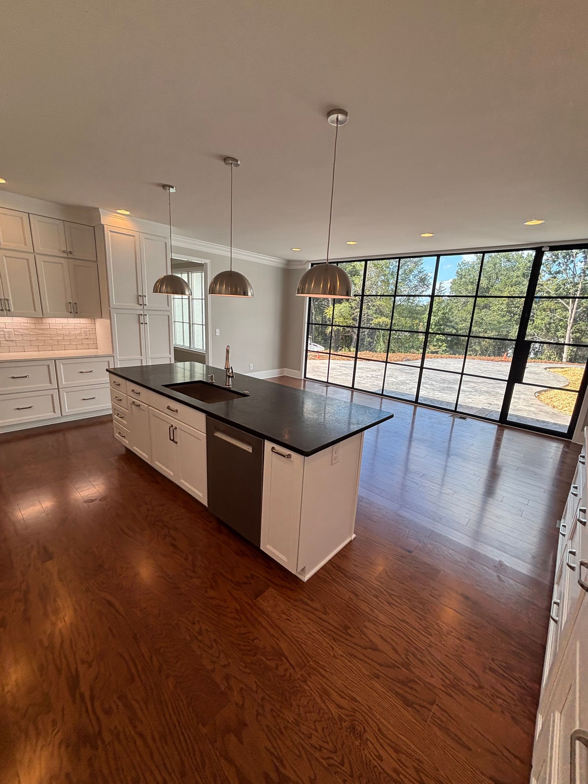 Modern kitchen with white cabinets, dark island countertop, and large windows overlooking trees.