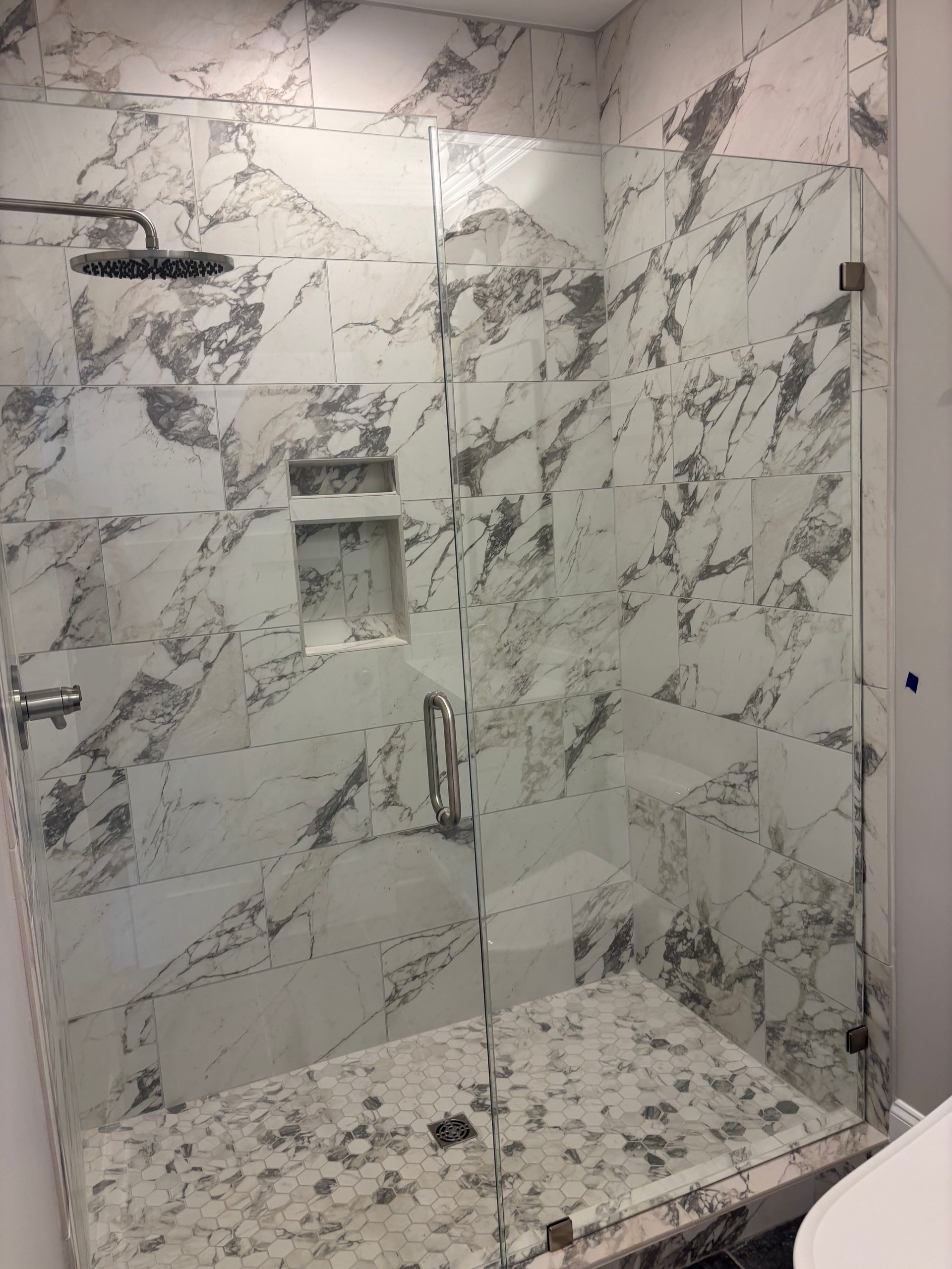 Marble-tiled shower with a glass door and a built-in shelf. Silver shower head and hardware.