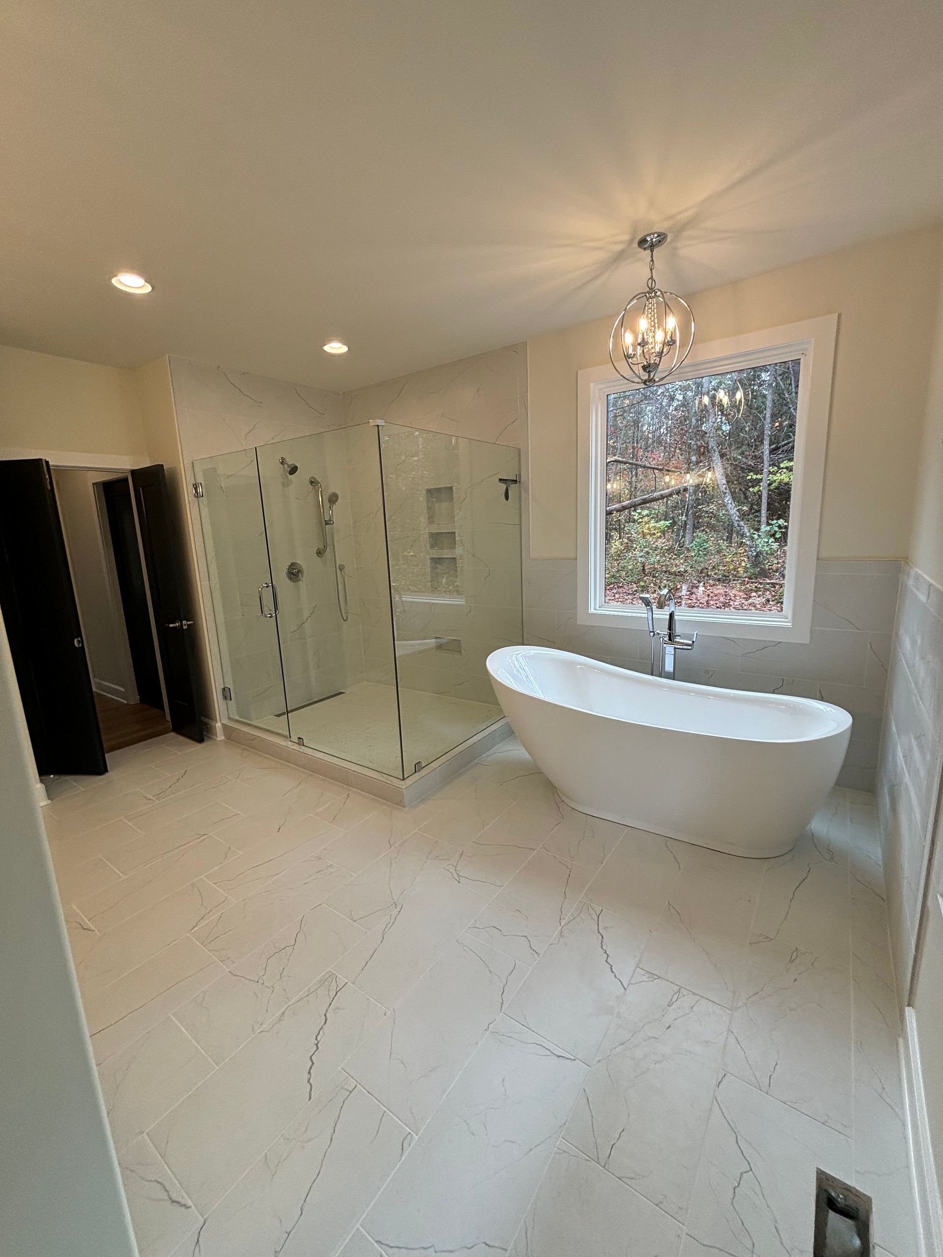 Modern bathroom with white freestanding tub, glass shower, and chandelier.
