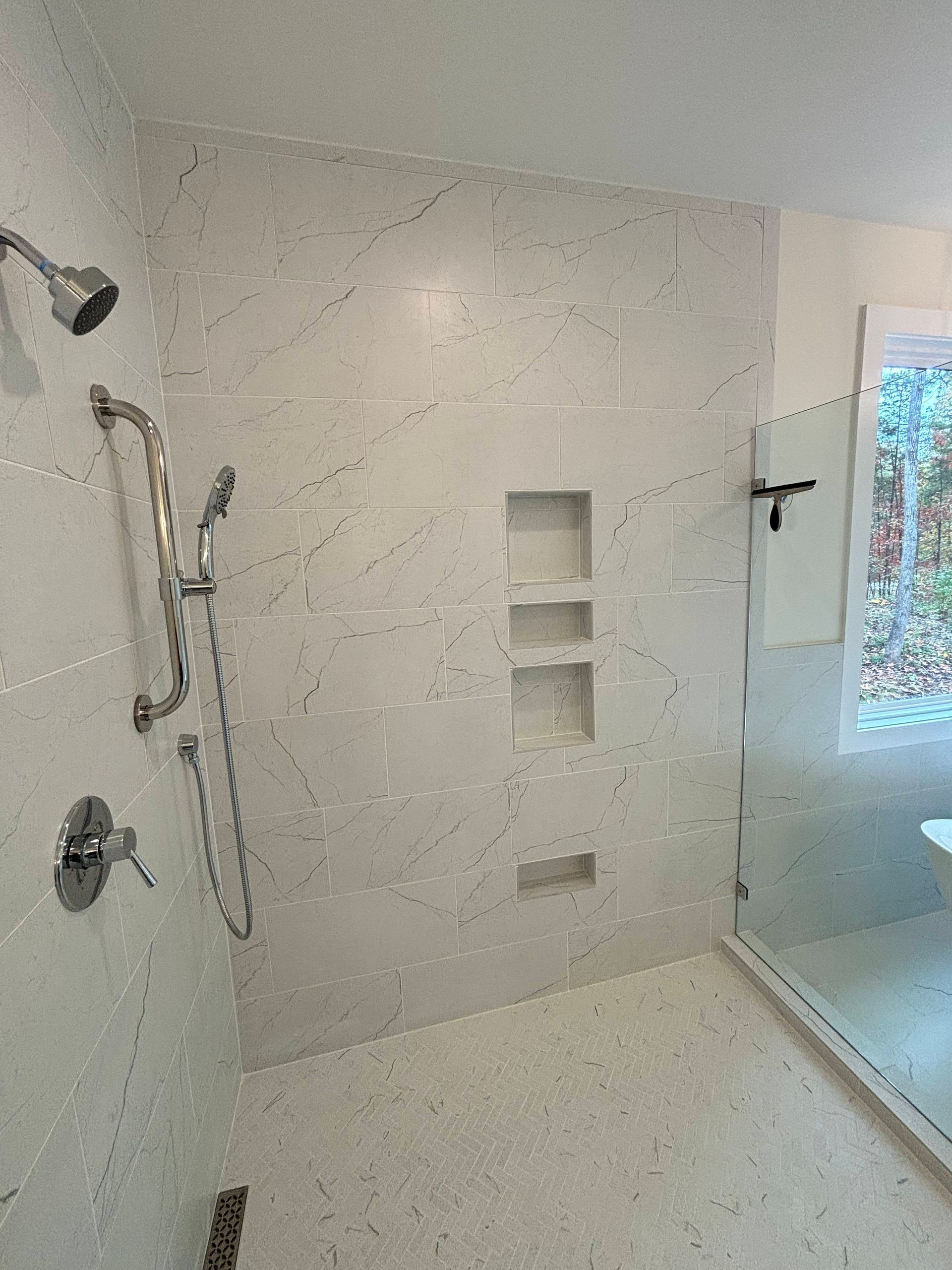 Bathroom shower with marble-like tile walls and a mosaic tile floor; stainless steel fixtures.