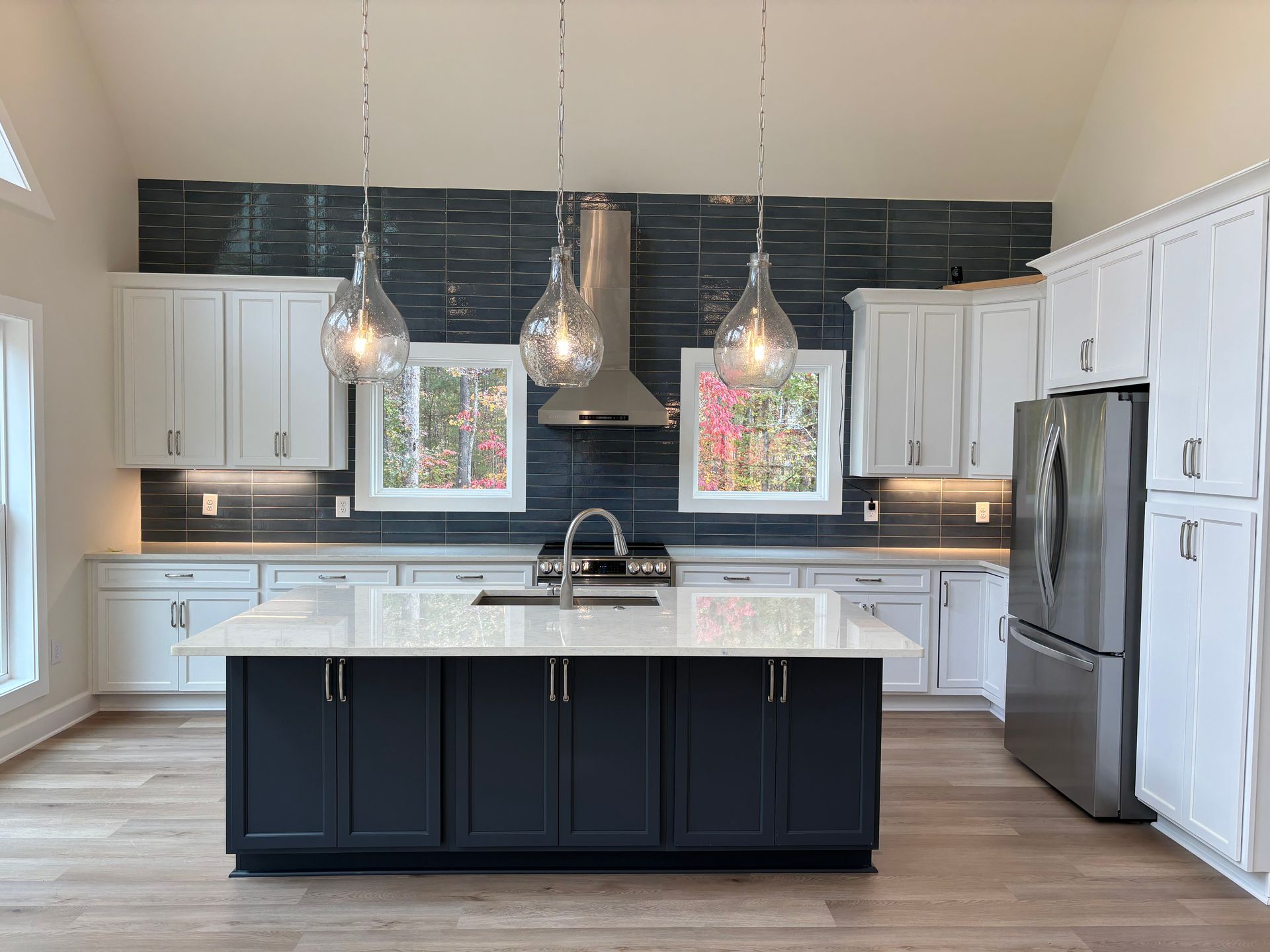 Modern kitchen with white cabinets, dark blue island, stainless steel appliances, and tile backsplash.