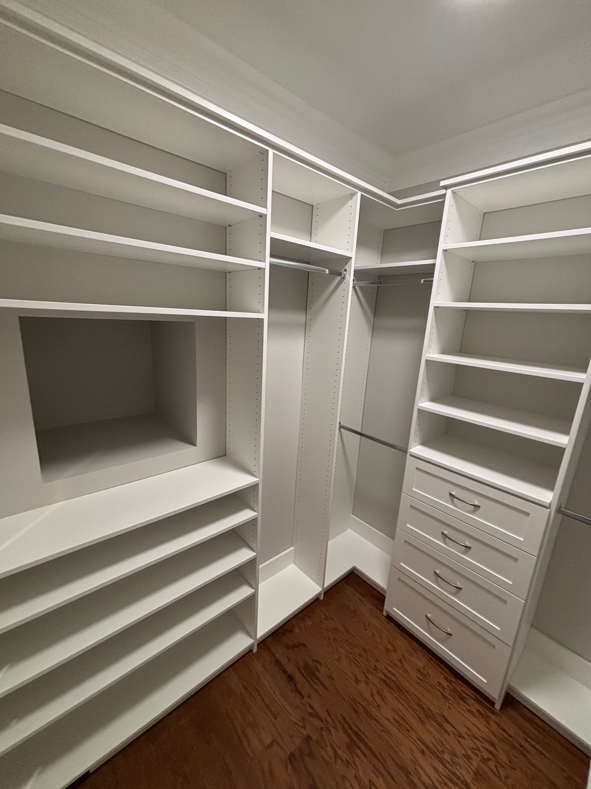 White custom closet with shelves, drawers, and hanging rods; hardwood floor.