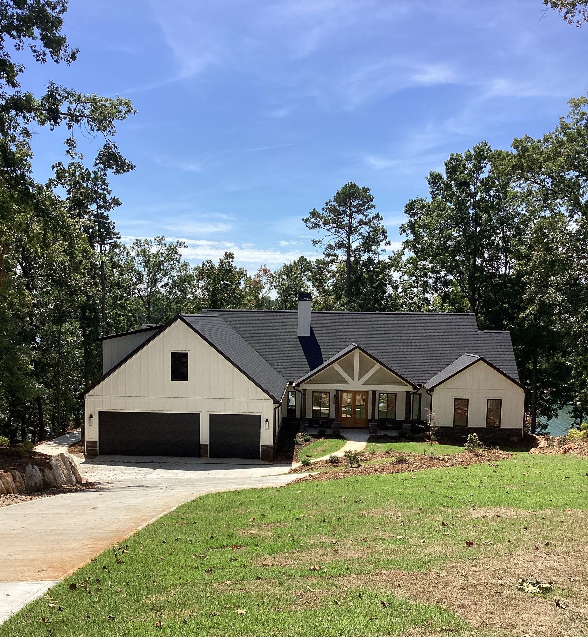 A white house with a black roof is surrounded by trees and grass.