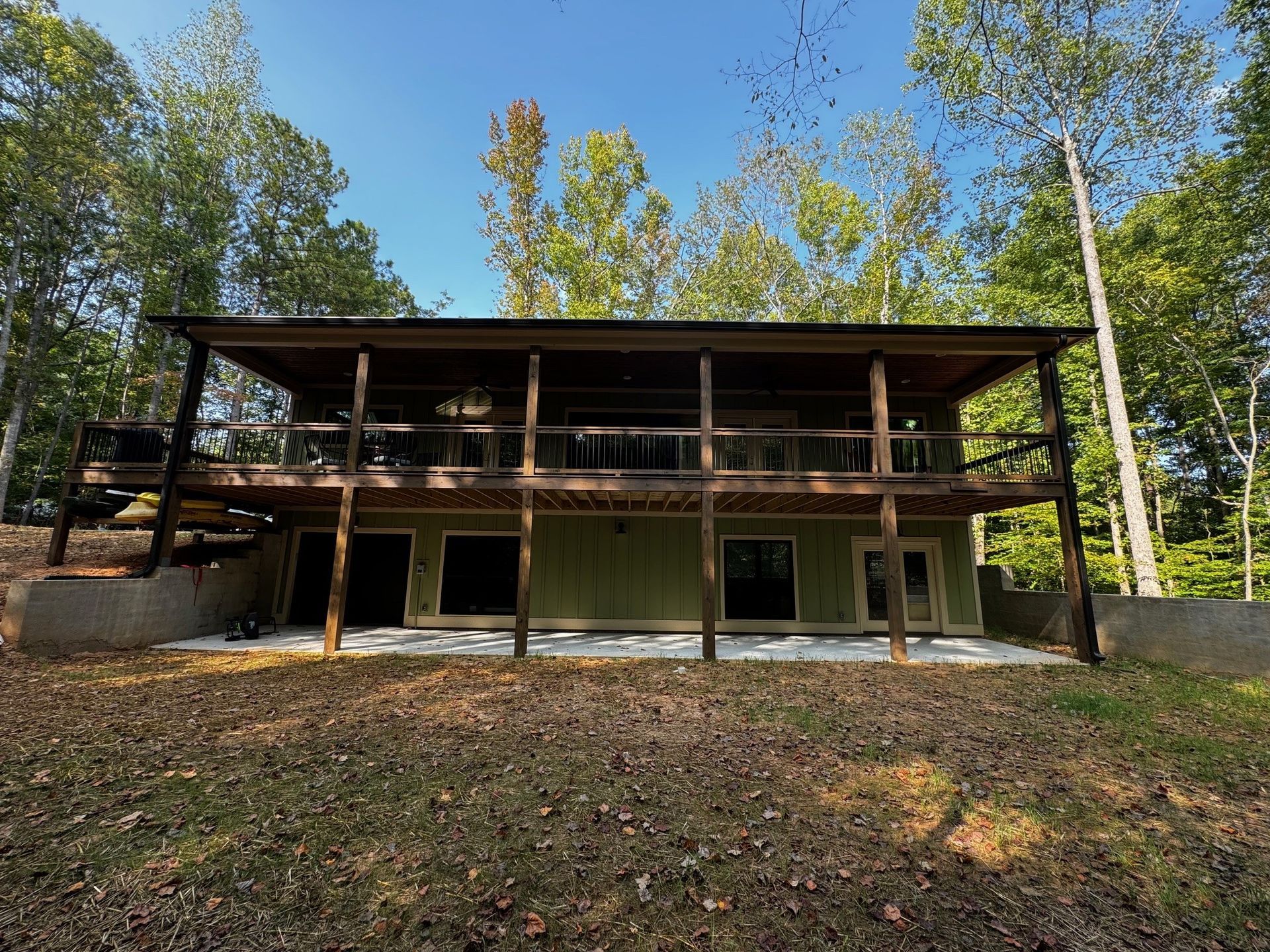 A large green house with a large deck is surrounded by trees.