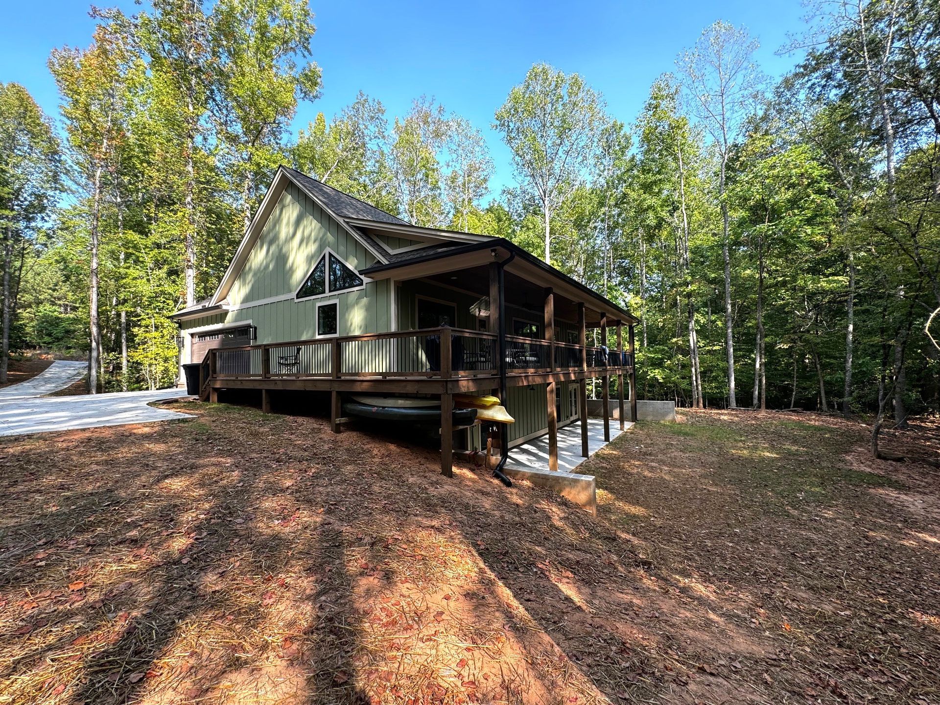 A green house with a large deck in the middle of a forest.