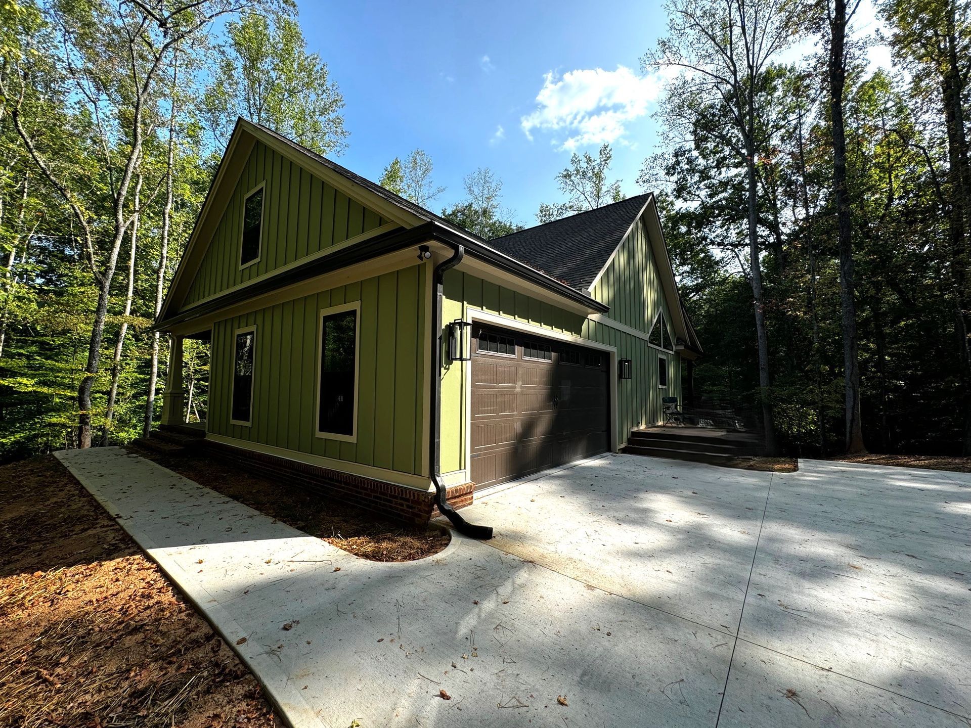 A green house with a brown garage door is surrounded by trees.