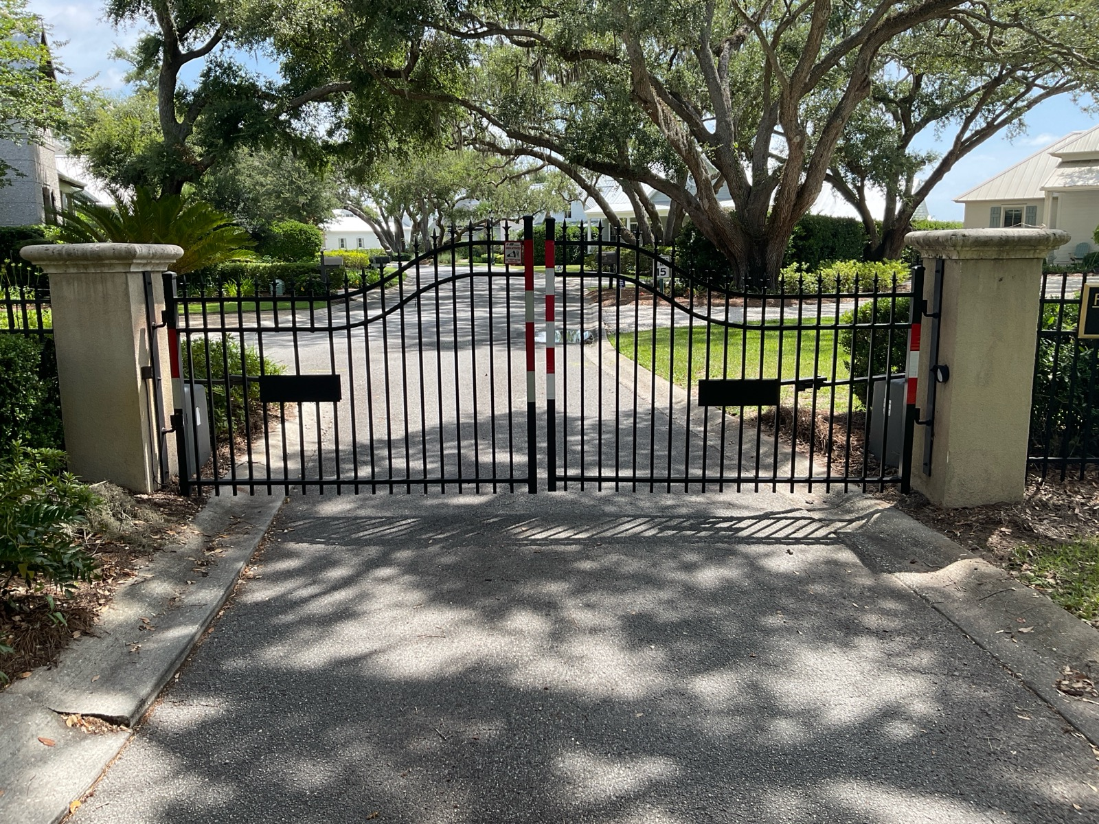 Black metal gate with stone pillars at a tree-lined driveway entrance.