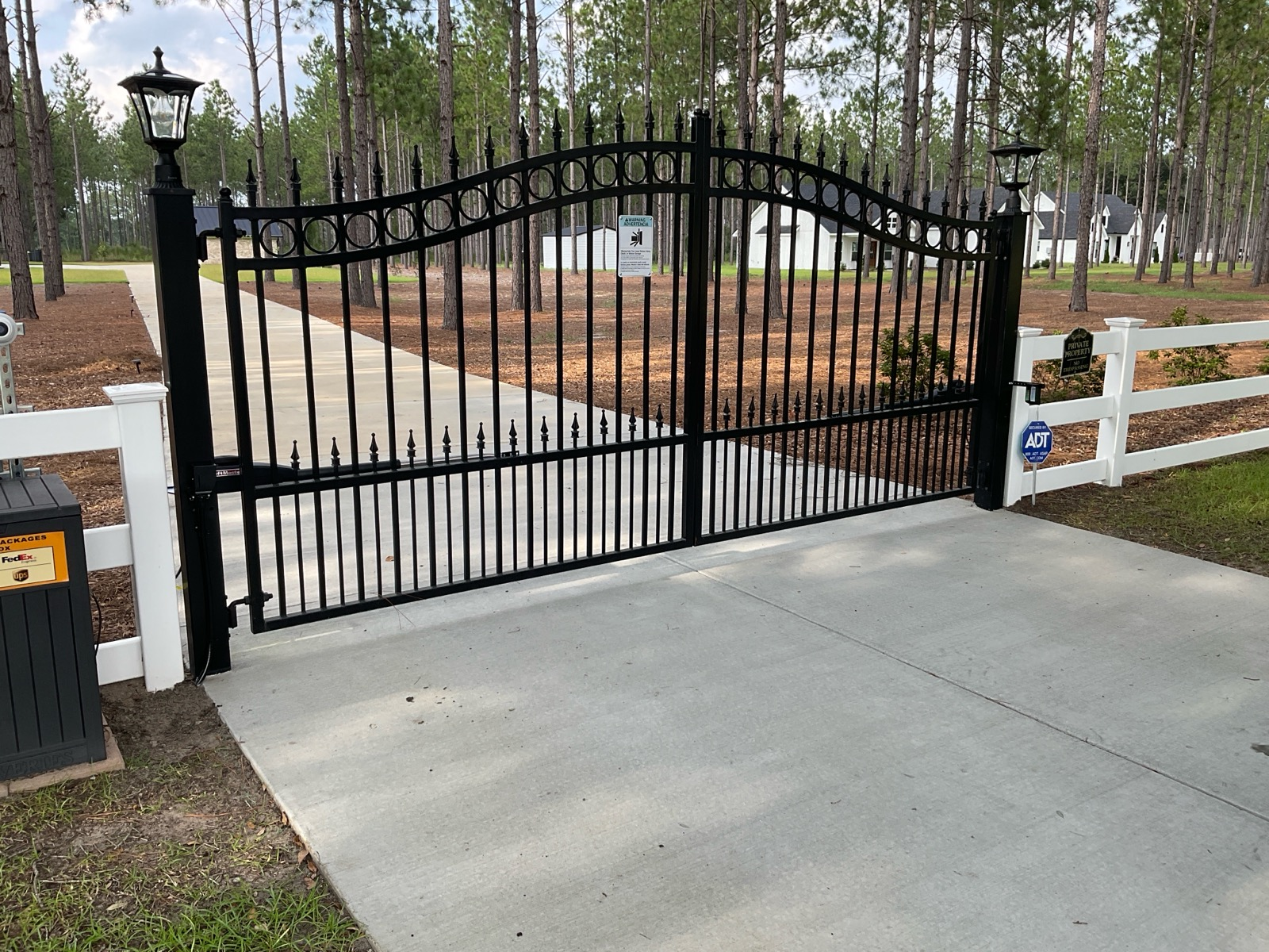 Black wrought-iron gate across a concrete driveway at a wooded entrance