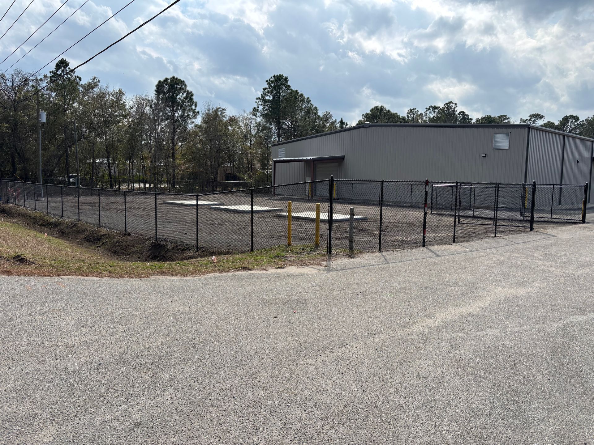 A fenced-in gravel lot with a gray building in the background and a cloudy sky.
