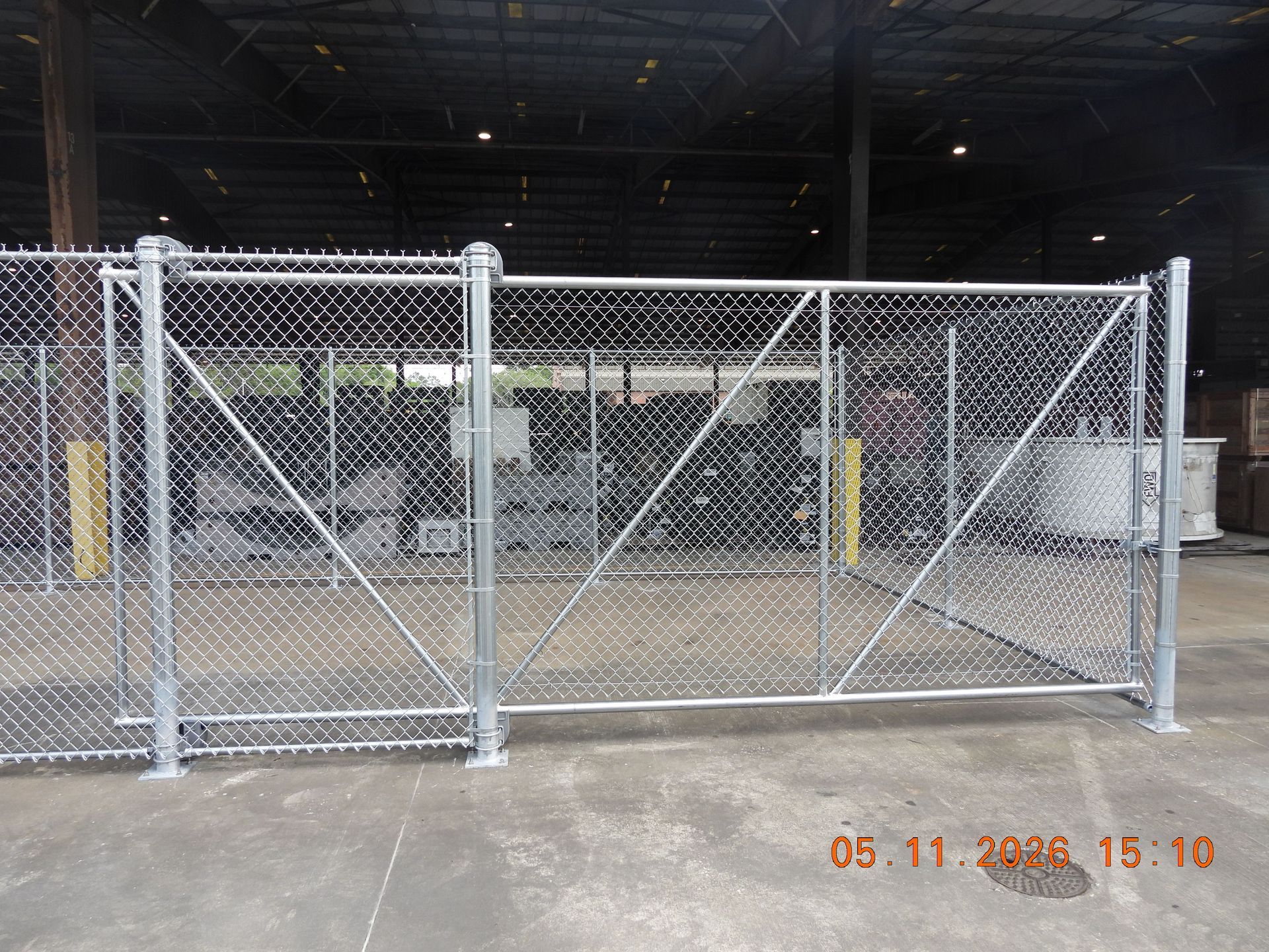 Chain-link security gate and fence in an industrial warehouse entrance, with yellow bollards behind it.