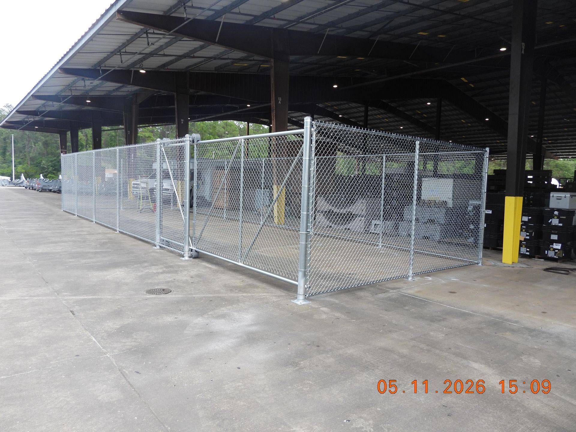 Chain-link fenced enclosure under a large metal warehouse awning on a concrete lot.