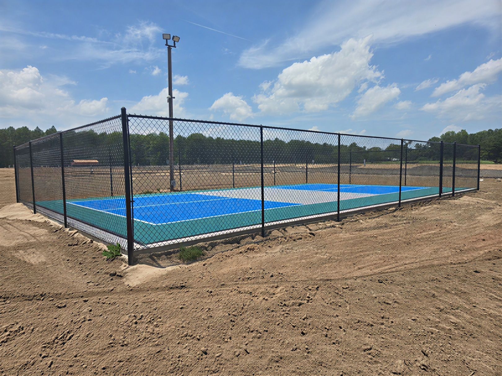 Fenced outdoor sports court with blue and tan surface under a cloudy sky