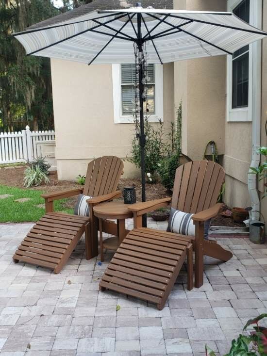 Patio seating area with two wooden lounge chairs, small table, and large umbrella on stone pavers